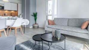 Un appartement moderne comprenant un coin repas, un canapé gris et une petite table ronde agrémentée de vases décoratifs.