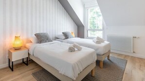 Une chambre moderne avec deux lits, un luminaire suspendu et une grande fenêtre.