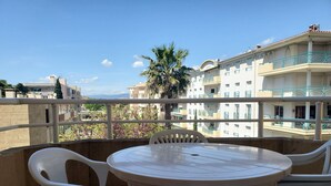 A balcony with a round table and four chairs, overlooking a building with balconies and a palm tree. - Port FREJUS Studio with sleeping area of ​​30 m2 for 2 Adults 2 Children with quiet balcony on the garden side (Fréjus)
