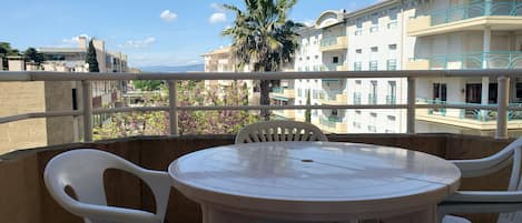 A balcony with a round table and four chairs, overlooking a building with balconies and a palm tree.