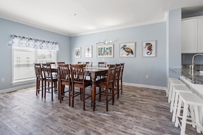 A dining room with a wooden table and chairs, a window with blinds, and artwork on the wall.