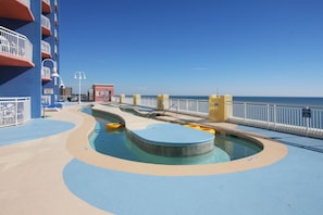 Un espace piscine doté d’une terrasse bleue et beige, de bouées jaunes flottantes et d’un poste de surveillance pour les sauveteurs.