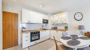 A modern kitchen with white cabinets, a wooden door, a built-in oven, a microwave, and a dining area with a round table and placemats. - Apartamenty Sun & Snow Bursztynowa (Sztutowo)