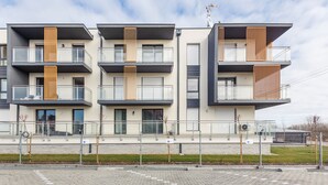 A modern multi-story residential building with balconies, a gated parking area, and a clear sky. - Apartamenty Sun & Snow Bursztynowa (Sztutowo)