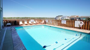 Une piscine d’un bleu éclatant, entourée d’une clôture en bois, avec des chaises longues et un poste de surveillance pour les sauveteurs.