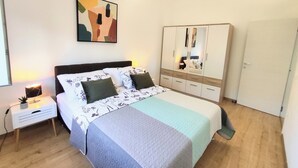 A bedroom with a bed, bedside table, lamp, wardrobe, and a painting on the wall.
