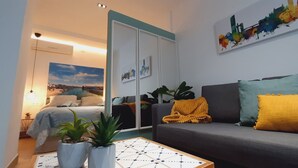 A modern living room with a grey sofa, yellow throw pillows, and a coffee table with a patterned table runner. There are two potted plants on the floor, a painting on the wall, and a cityscape artwork above the sofa. - Lovely penthouse apartment with terrace Lovely Center Apartments Alameda (Sevilla)