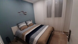 Une chambre à coucher avec un lit, des coussins à rayures, une fenêtre avec des rideaux légers et un mur décoré d’autocollants représentant des poissons.