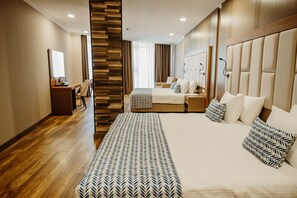 A modern hotel room with a large bed, a desk, a chair, and a wardrobe.