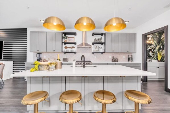 Una cocina moderna con una isla central, taburetes de bar, iluminación colgante y vistas al exterior.