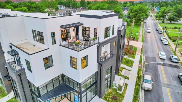 Un edificio moderno de varios pisos con patio en la azotea, ventanas amplias y vista a la calle.