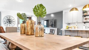 Una cocina moderna con una mesa de madera, tres jarrones de vidrio y un reloj grande en la pared.