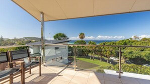 Un balcone con ringhiera in vetro che si affaccia su un paesaggio verdeggiante e vista sull'oceano.