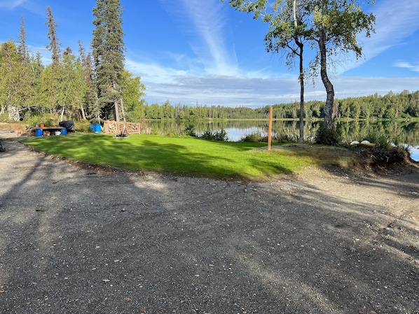 Un terrain de camping doté d’un parking en gravier, d’un champ herbeux et d’un lac.