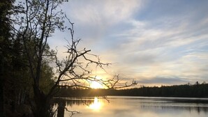 A calm lake with a sunset in the background, surrounded by trees and a forested area. - Private Lake Front with boat launch and dock. (Kenai)