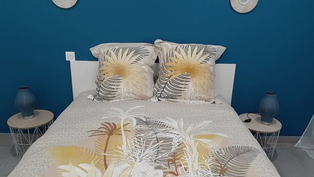 Un dormitorio con una cama, dos almohadones decorativos, dos mesitas de noche y dos jarrones.