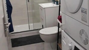Un baño pequeño con cabina de ducha de vidrio, inodoro blanco y lavadora y secadora apiladas.