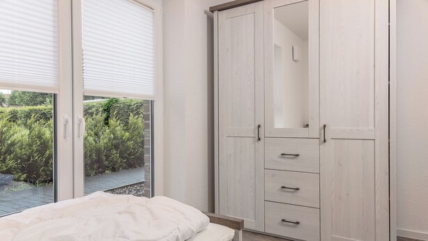 Ein Schlafzimmer mit einem Bett, einem Kleiderschrank und Blick auf Grünfläche.