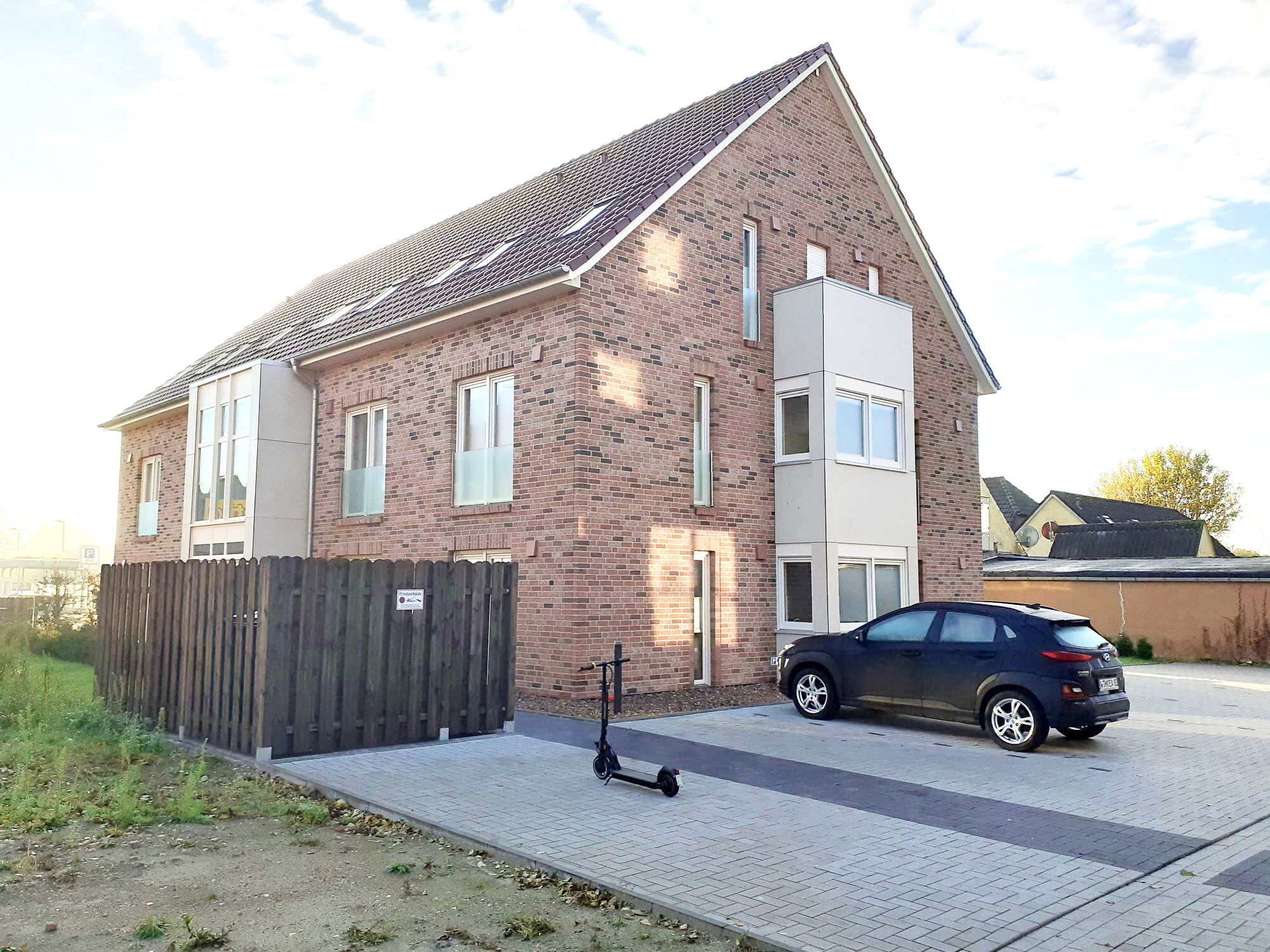 A two-story brick house with a car parked in the driveway and a scooter on the sidewalk.