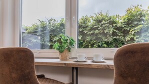 Ein Zimmer mit Fenster, einem Holztisch, zwei Stühlen und einem Blumentopf.