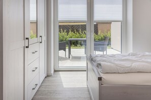 A bedroom with a bed, a sliding door leading to a balcony, and a small table with chairs. - First floor apartment with double terrace (new build from 2022) in a top location (Carolinensiel)