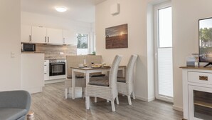 Eine moderne Küche mit weißen Schränken, einer Mikrowelle und einem Backofen. Ein Esstisch mit Stühlen und ein Bild an der Wand sind ebenfalls vorhanden.