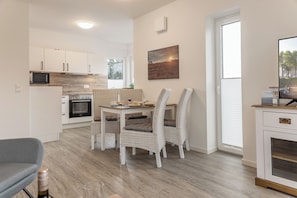 Une cuisine moderne avec des meubles blancs, un four à micro-ondes et un four traditionnel. On y trouve une table à manger avec des chaises et un tableau accroché au mur.