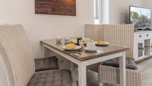 Ein Essbereich mit Korbmöbeln, einem Tisch gedeckt mit Tellern, Tassen und einem Fernseher, der eine Stadtansicht zeigt.