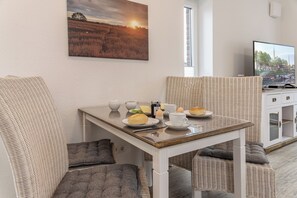Un coin repas avec des meubles en osier, une table dressée avec des assiettes, des tasses et un téléviseur diffusant une vue sur la ville.