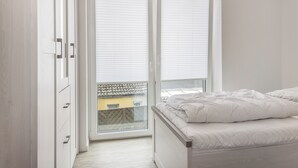 A bedroom with a bed, a sliding glass door to a balcony, and a white wardrobe. - Apartment (Carolinensiel)