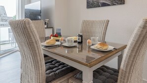 A dining area with wicker chairs, a wooden table, and breakfast items. - Apartment (Carolinensiel)