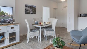 A modern living room with a dining area, white wicker furniture, a television, and a plant. - Apartment (Carolinensiel)