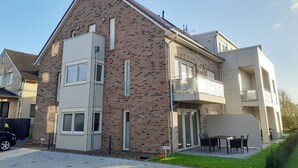 A modern two-story residential building with a brick facade, large windows, and a balcony. - Apartment (Carolinensiel)