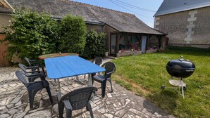 Eine Terrasse mit blauem Tisch und Stühlen, einem Grill und einem Boden aus Steinplatten.