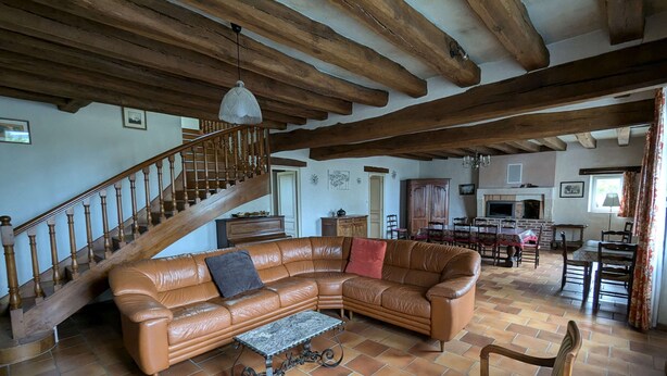 Ein geräumiges Wohnzimmer mit einem ledernen Ecksofa, einem Holztisch und einem Sessel. Eine Holztreppe mit Geländer führt zu einer weiteren Ebene.