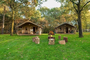 Two rustic cabins with wooden decks and a central fire pit surrounded by tree stumps. - EuroParcs Ruinen (Ruinen)