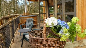 A wooden deck with outdoor furniture, a wicker basket with flowers, and a building with large windows. - EuroParcs Ruinen (Ruinen)