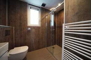 A bathroom with a wooden wall, a toilet, a glass shower enclosure, and a white towel rack. - EuroParcs Ruinen (Ruinen)