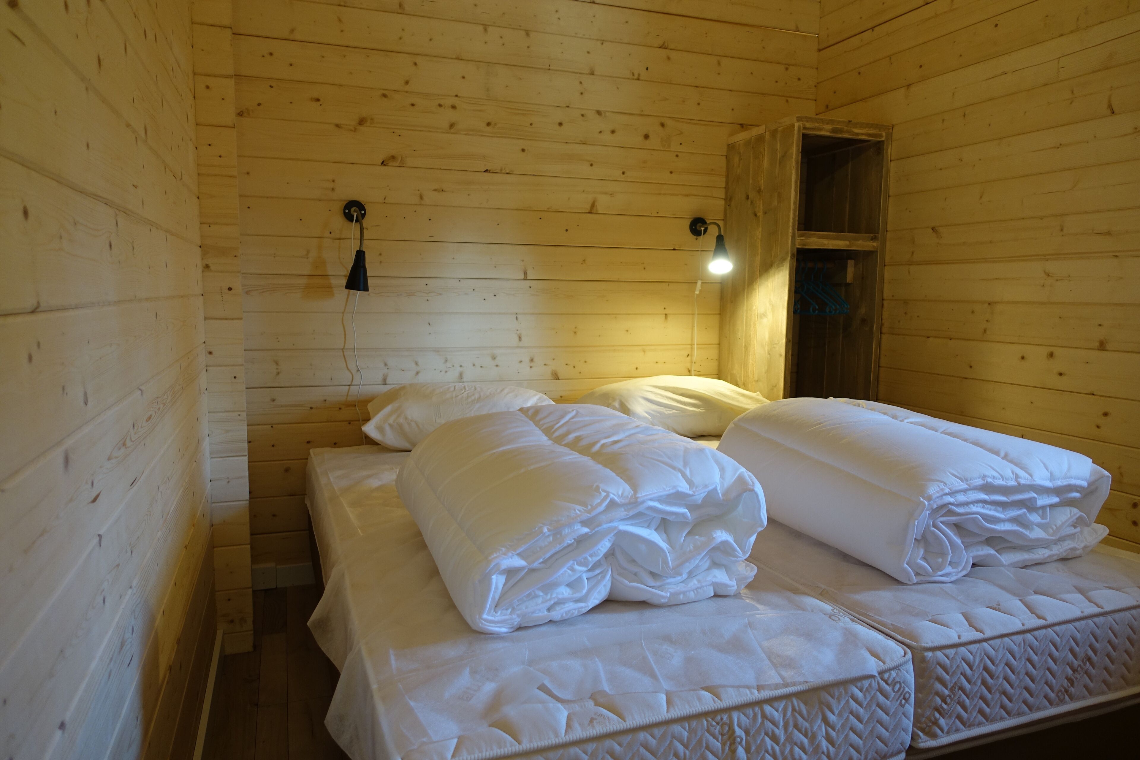 Une chambre dans un chalet en bois, avec deux lits, chacun recouvert de draps blancs soigneusement pliés.
