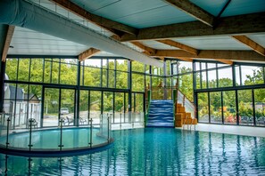 An indoor swimming pool with clear glass walls, a slide, and a view of the surrounding greenery. - EuroParcs Ruinen (Ruinen)
