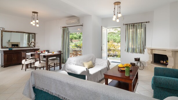 A spacious living room with a fireplace, a dining area, and a view of the garden. - Haris Villas (Viannos)