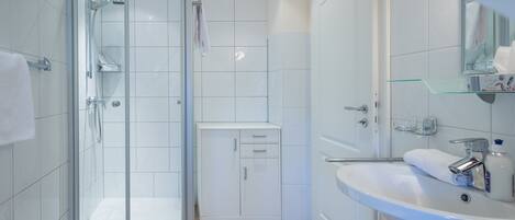 A modern bathroom with a glass shower enclosure, a white sink, and a small cabinet.