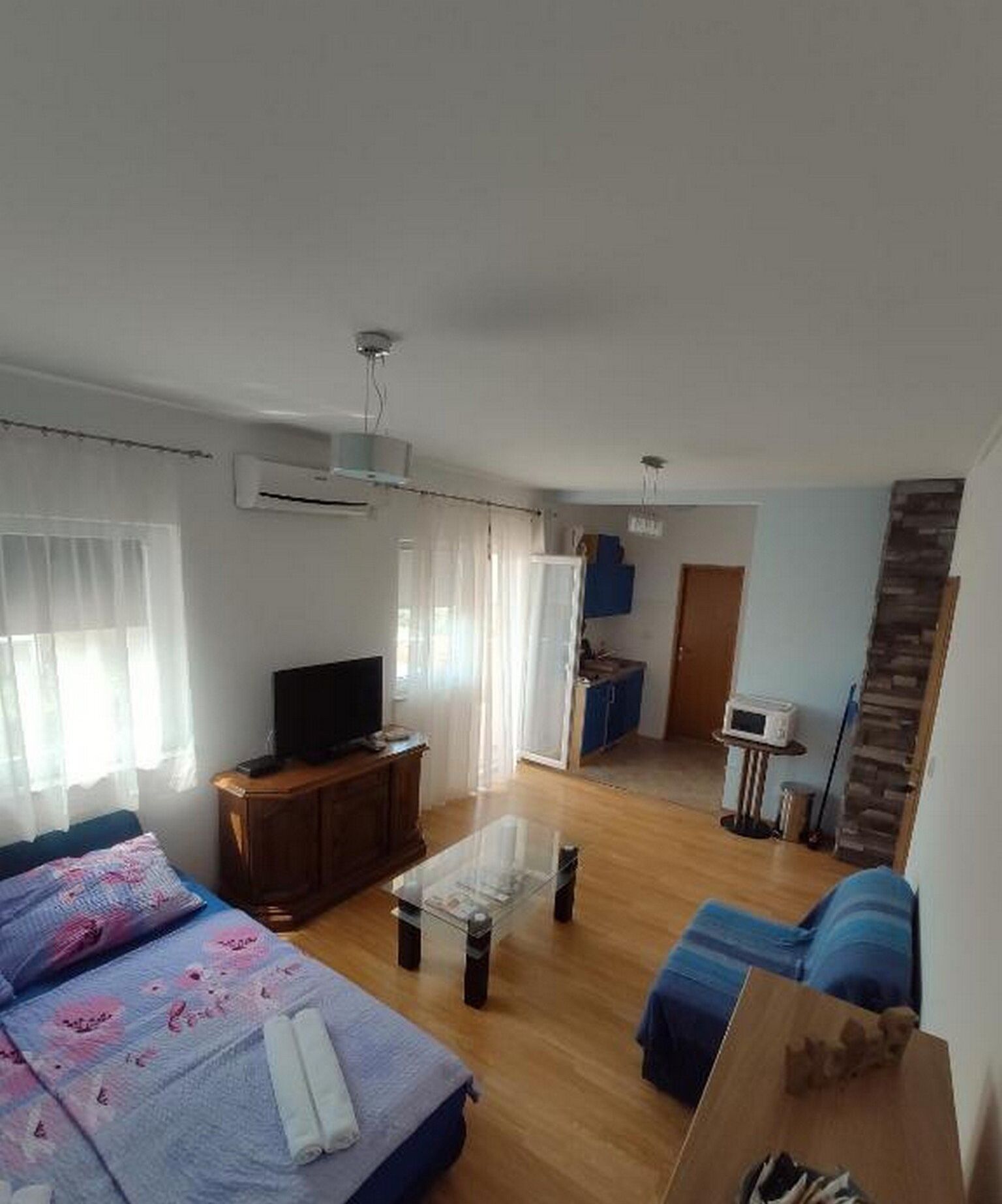 Una sala de estar moderna con un sofá, una mesa de centro y un televisor. Se observa una cocina al fondo con un microondas y armarios.