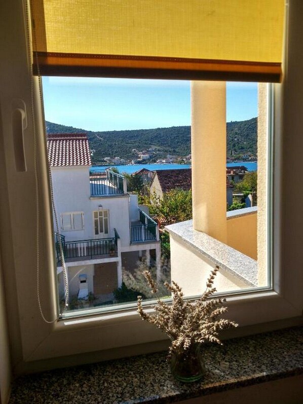 A window with a view of a coastal town, a balcony, and a small vase with dried flowers. - Apartments Vala (Marina)