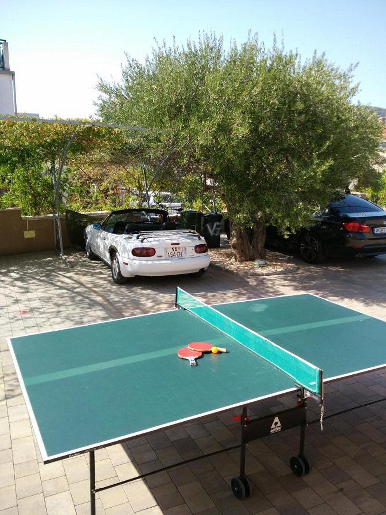 Un tavolo da ping pong in un'area esterna, con un'auto parcheggiata nelle vicinanze.