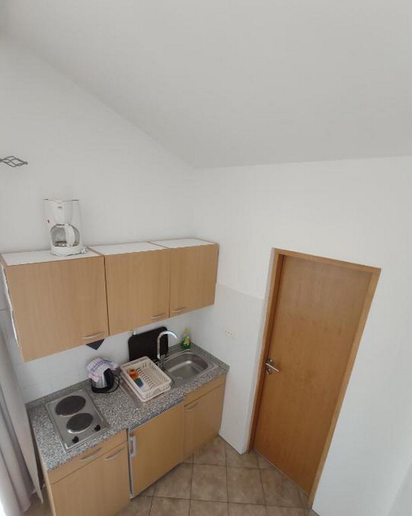A compact kitchen with wooden cabinets, a granite countertop, a coffee maker, and a sink.