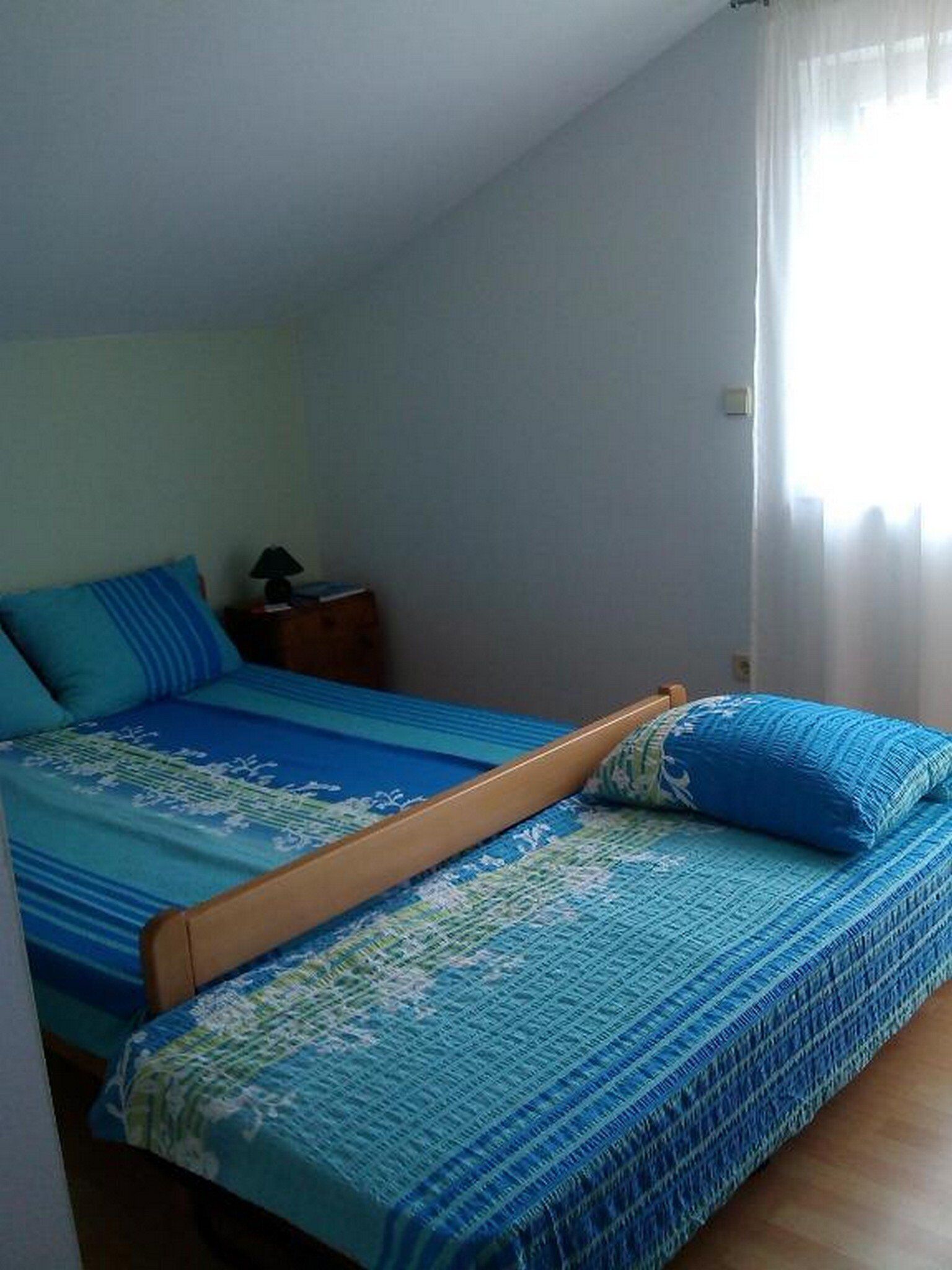 A single bed with blue bedding in a room with a sloped ceiling.