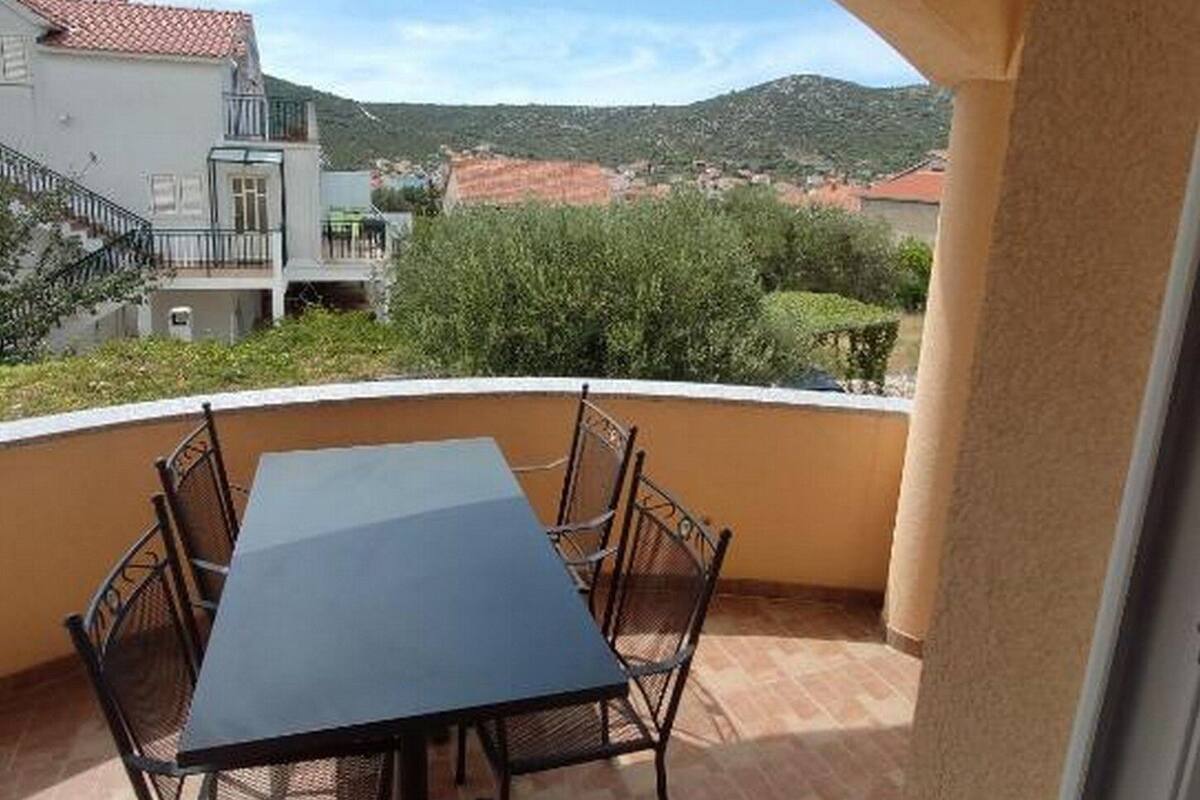 Un balcon avec une table et des chaises, donnant sur un quartier résidentiel avec des maisons et des collines.
