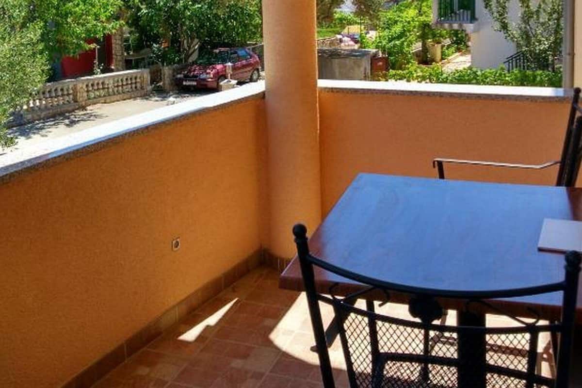Un balcon avec une table et des chaises, donnant sur un quartier résidentiel avec des maisons et de la verdure.