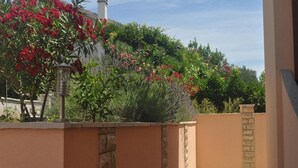 Un jardín con diversas plantas y flores, un farol de metal y un muro de piedra.